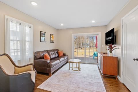 A warm living room featuring a brown leather sofa, a round coffee table, and sliding glass doors to the outdoor patio.