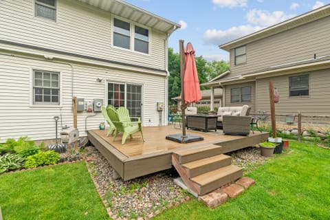 Backyard deck with green chairs and brown wicker seating under a rust-colored umbrella.