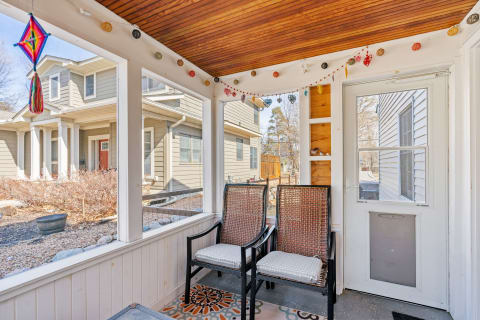 A cozy screened porch featuring wicker chairs, colorful lights, and a view of the yard.