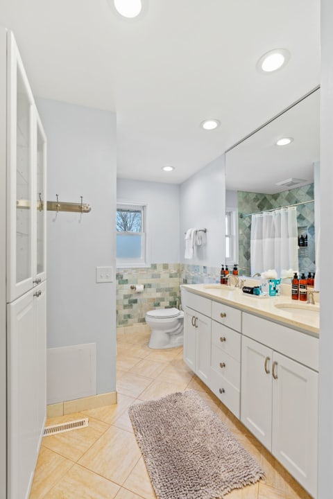 A bright and modern bathroom featuring a dual sink vanity, mosaic tile backsplash, and light gray walls.