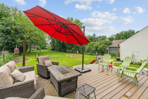 Patio with a red umbrella, cozy seating, and a green lawn in the background.
