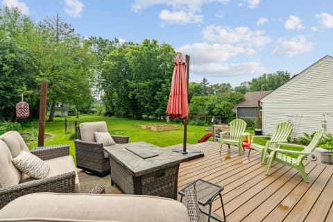A spacious deck with stylish seating and a patio umbrella set in a vibrant green backyard.