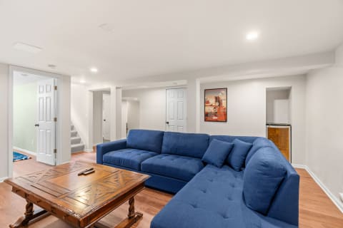 A stylish basement featuring a navy blue sectional couch, rustic coffee table, and light-colored walls.