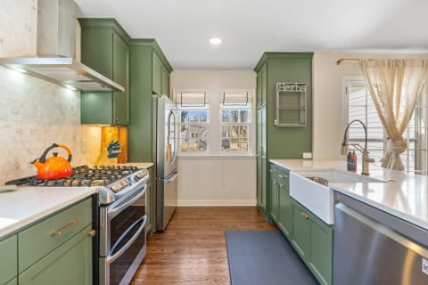 Modern kitchen with green cabinets and orange kettle on the stove.