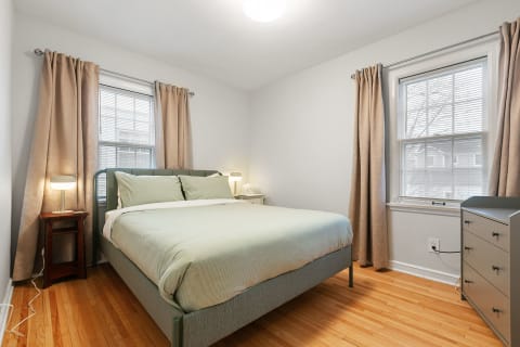 Cozy bedroom with green bedding, curtains, and a wooden bedside table.