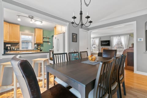 A dining room connecting to a kitchen, featuring a dark wooden table, orange centerpiece, and light cabinets in the background.