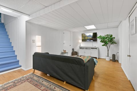 A modern basement living area featuring a gray sofa, TV, and blue stairs leading up.