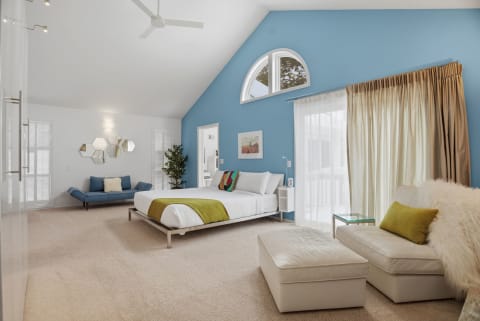 Spacious bedroom featuring a high ceiling, blue accent wall, and warm seating area.