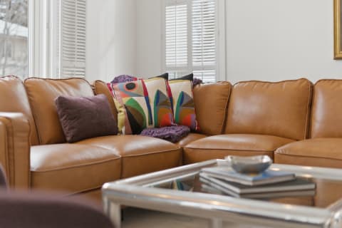 A plush leather sectional sofa with decorative pillows and a throw blanket next to a coffee table in a bright living room.