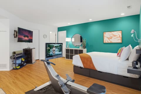 A spacious bedroom featuring a teal wall, bed, fitness rowing machine, and modern decor.