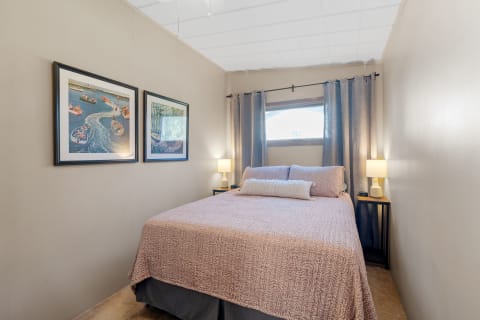 Cozy bedroom featuring a bed with pink bedding, two framed artworks, and a nightstand with a lamp.