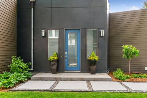Stylish entrance with a blue front door, black planters, and green landscaping.