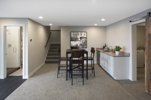 Interior view of a modern basement with a dining area, kitchenette, and staircase.