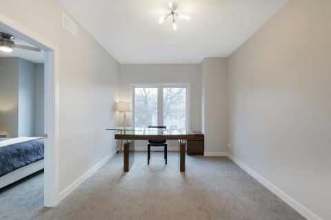 A sleek, modern workspace featuring a glass desk, black chair, and natural light from a large window.