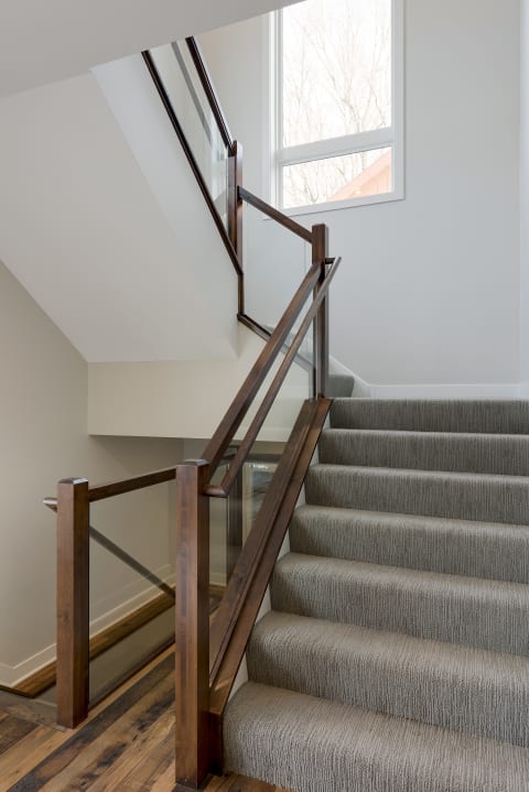 Interior view of a modern staircase with a wooden railing and grey carpet.