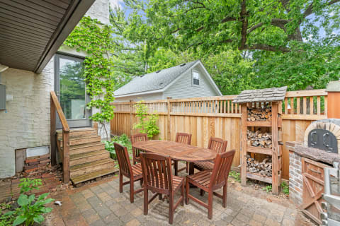 Outdoor patio area with a wooden table and chairs, ivy-covered wall, and nearby log storage.