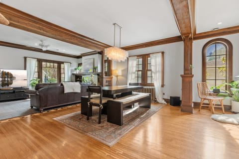 A warm living room and dining area with wooden beams, leather couch, and a stylish chandelier.