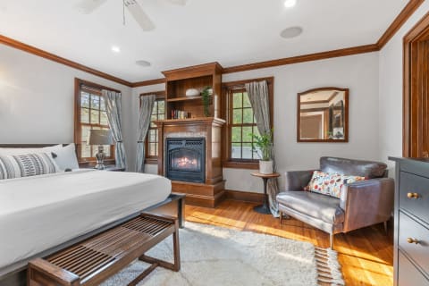 A well-decorated bedroom featuring a bed, armchair, and a fireplace.