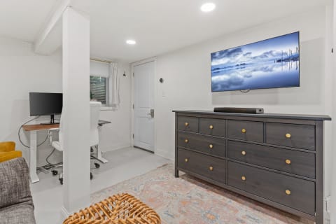 Cozy basement room with modern furniture including a sofa, dresser, and work desk.