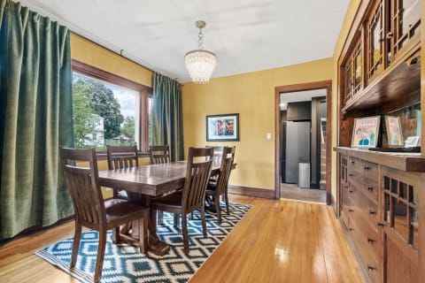 Interior view of a dining room featuring a wooden dining table, chandelier, and green curtains.