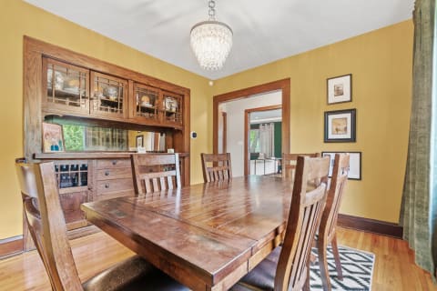 A spacious dining room featuring a wooden table, chairs, and a chandelier under golden-yellow walls.