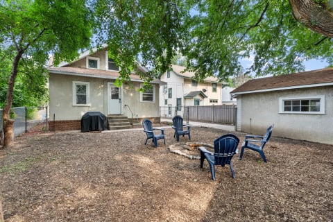 A backyard featuring a fire pit surrounded by blue chairs and a cozy house in the background.