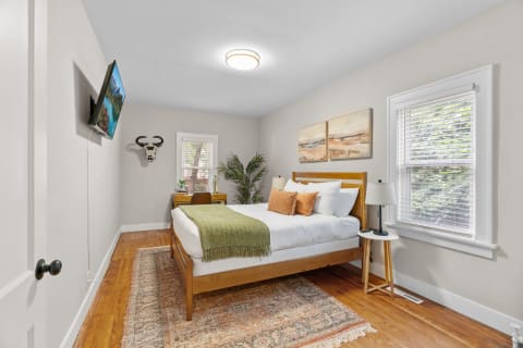 Cozy bedroom featuring a bed with white linens, decorative pillows, and a mounted TV.