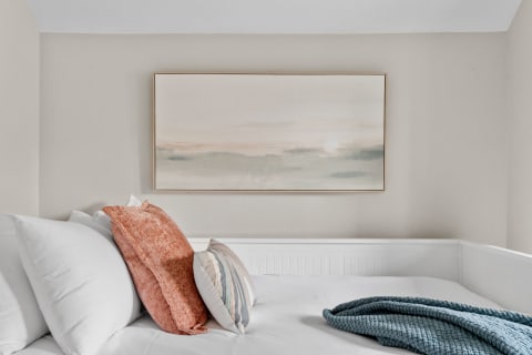 A cozy bedroom corner featuring decorative pillows and an abstract landscape painting.