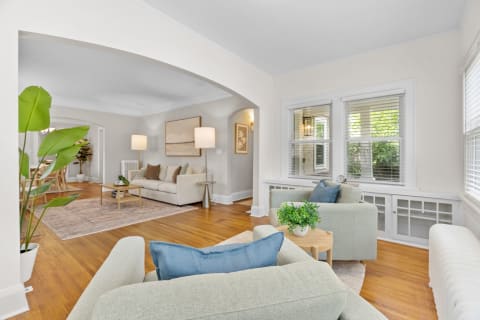 A cozy living room featuring light green armchairs, a beige sofa, and natural greenery.