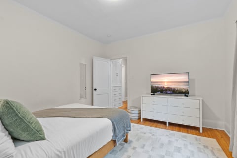 A well-furnished bedroom featuring a neatly made bed, a television, and a white dresser.
