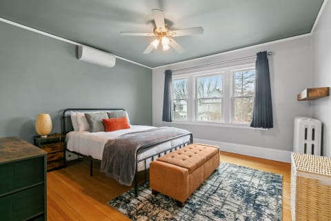 A stylish bedroom featuring a black metal bed, orange accents, and a calming gray color palette.