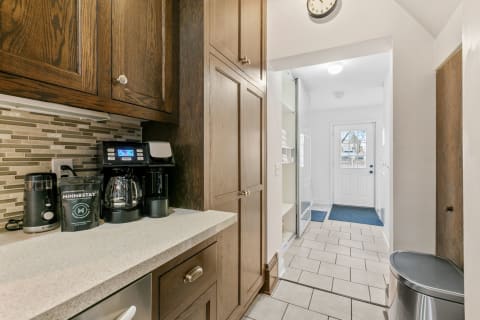 A view of a modern kitchen with dark wood cabinets and a coffee-making corner, leading into a hallway with a door to the outside.