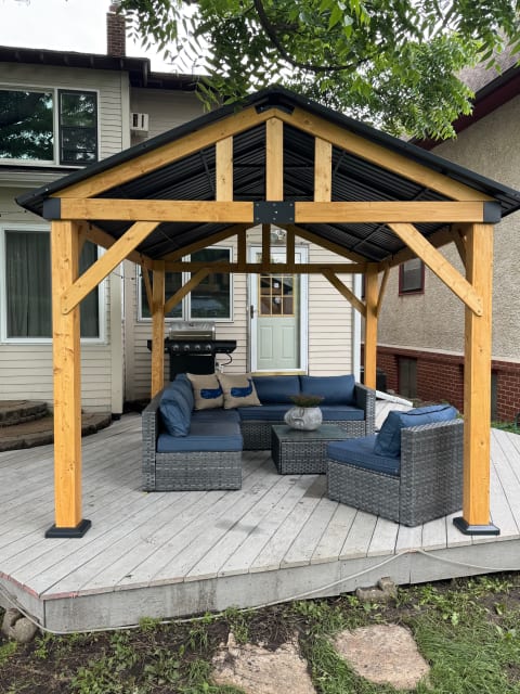 Outdoor gazebo with comfortable seating and a nearby grill.