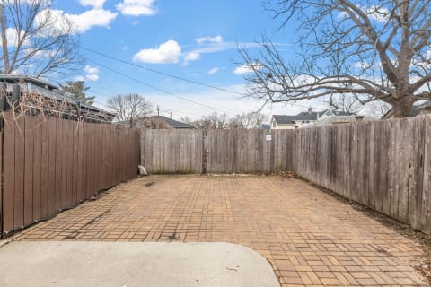 A spacious fenced outdoor area with a brick patio and a clear sky above.