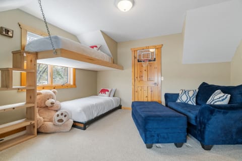 A children's bedroom with a lofted bed, plush teddy bear, blue couch, and a basketball hoop on the door.