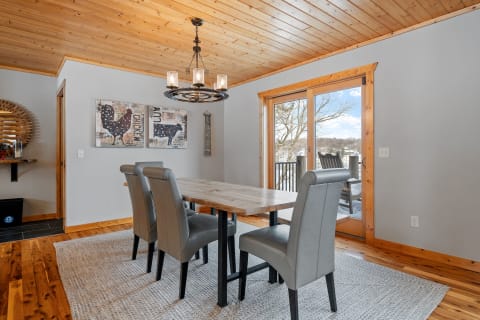 A cozy dining room featuring a wooden table, gray chairs, and bright outdoor view through glass doors.