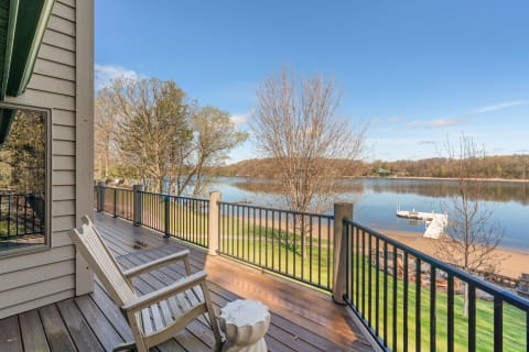 A wooden deck overlooking a calm lake with a rocking chair and trees.