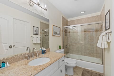 Modern bathroom with granite countertops, white cabinetry, and a glass shower.
