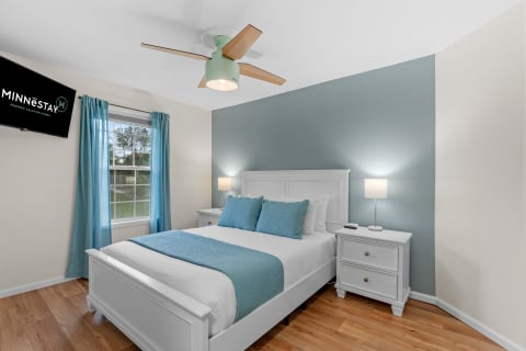 A serene bedroom featuring a bed with turquoise pillows, white nightstands, and a ceiling fan.