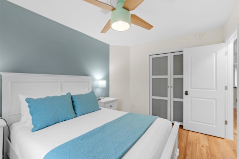 Cozy bedroom featuring a white bed with blue pillows, a teal accent wall, and modern furnishings.