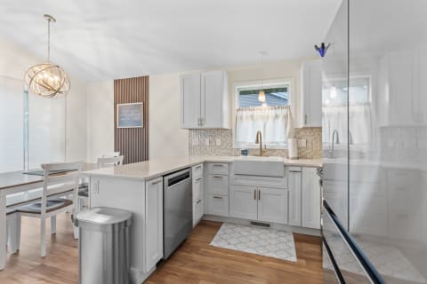 Modern kitchen with white cabinetry, pendant lighting, and wooden flooring.