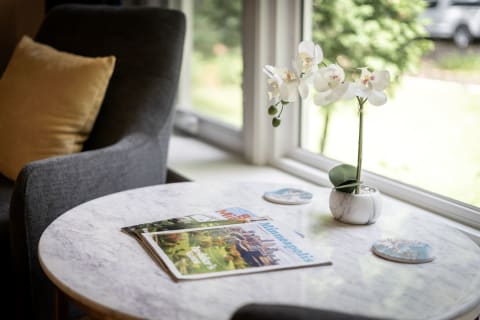 A round marble table with magazines and a white orchid in a pot, beside a gray armchair.
