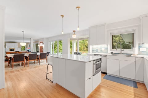 A spacious modern kitchen and dining area showcasing white cabinetry, a large island, and large windows overlooking greenery.