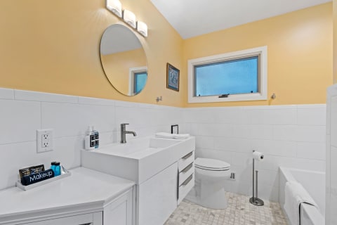 A bright and modern bathroom with white and yellow decor, featuring a vanity, mirror, and bathtub.