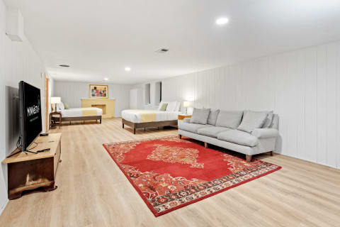 A spacious room featuring two beds, a sectional sofa, a red area rug, and a TV on a console.