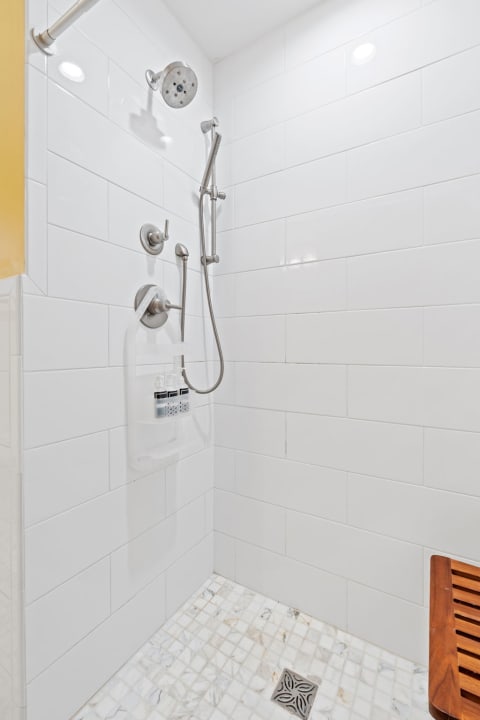 Contemporary shower space with white tiles, chrome fixtures, and a wooden stool.