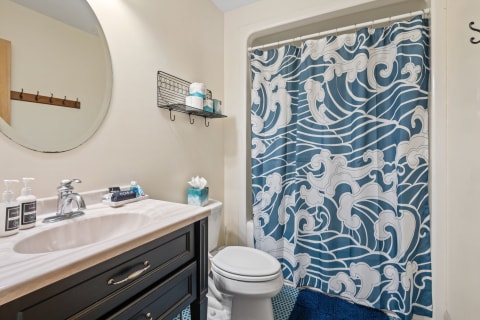 Compact bathroom featuring a wave-patterned shower curtain and modern black vanity.