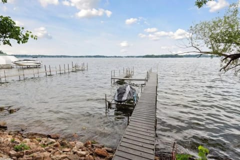 Lakeside view featuring a wooden dock, covered boat, and rocky shoreline.