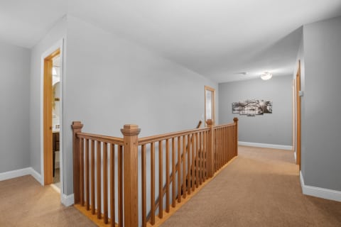 An upper hallway with a wooden railing, light gray walls, and beige carpeting.