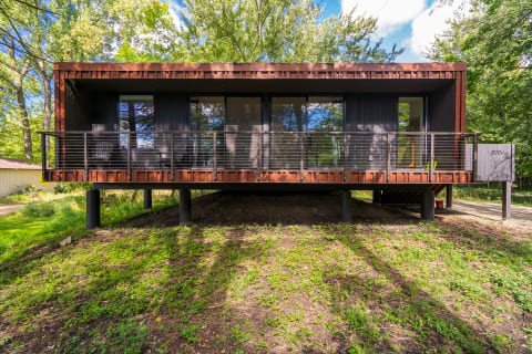 A contemporary elevated house with large windows and a spacious deck, surrounded by trees.